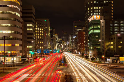 Light trails over street amidst illuminated buildings at night