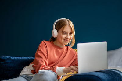 Smiling teenage girl wearing headphones typing on laptop