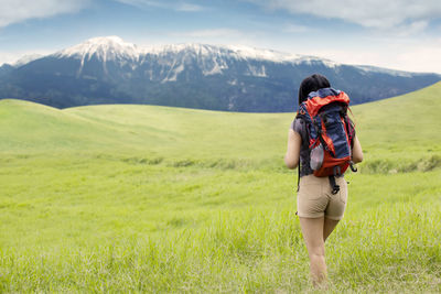 Rear view of backpacker walking on field against mountains