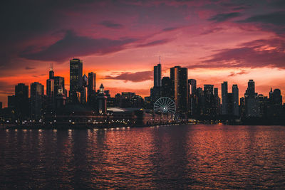 Buildings by lake against sky at dusk