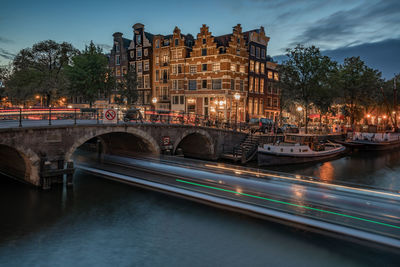 Illuminated bridge over river in city against sky at dusk