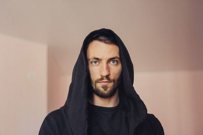 Portrait of man wearing hooded shirt against wall