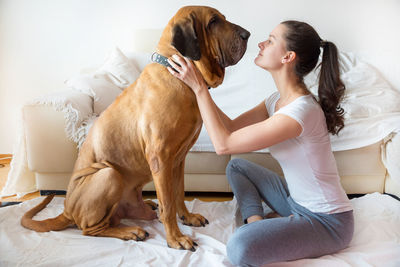 Side view of young woman face to face with dog sitting on bed at home
