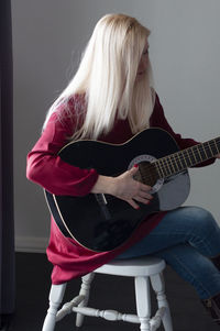 Beautiful young blonde woman in a red dress with a black guitar, favorite hobby