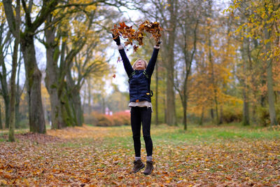 Woman playing with leaves in forest during autumn