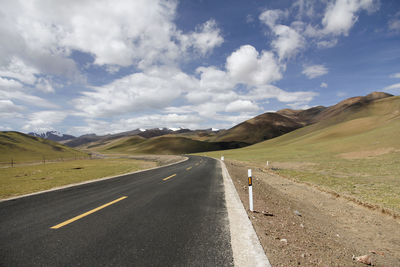 A flat, wide asphalt road leads to the beautiful and spectacular snow mountains in the distance