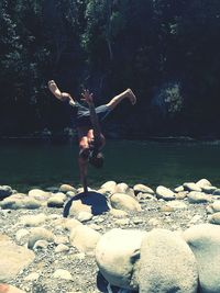 Shirtless young man doing handstand at lakeshore