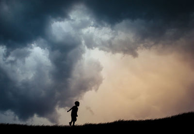 Silhouette of woman on field against cloudy sky