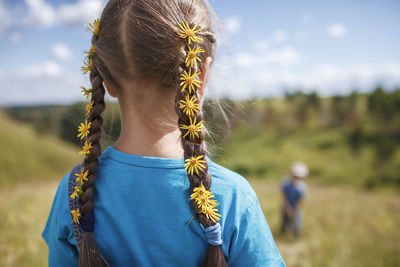 Rear view of girl wearing flowers in hair while standing on field