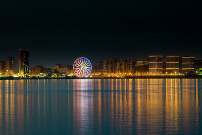 Illuminated ferris wheel in city against sky at night