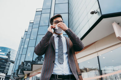 Business man with protective face mask using phone on city street.