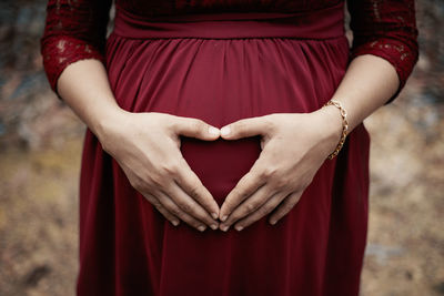 Midsection of pregnant woman making heart shape on stomach 