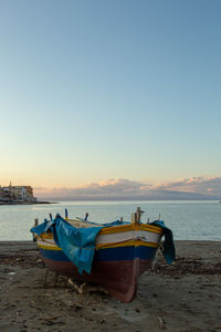Boat moored on shore against sky during sunset