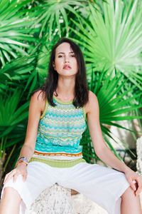 Portrait of young woman sitting against plants