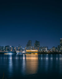 Illuminated buildings by river against sky at night