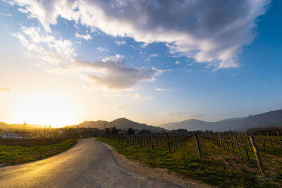 Road amidst field against sky during sunset