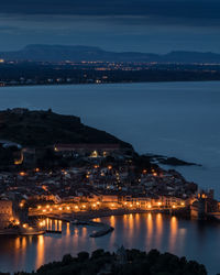 High angle view of illuminated buildings by sea against sky at night