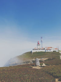 Lighthouse on field by buildings against sky