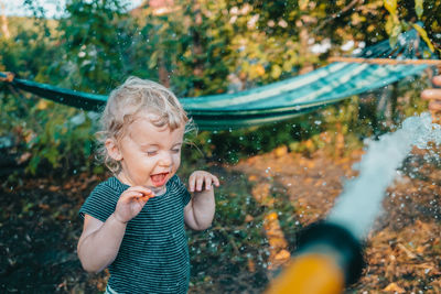 Cute boy standing at yard playing with garden hose water