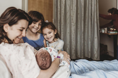 Side view of mother holding newborn son meeting siblings