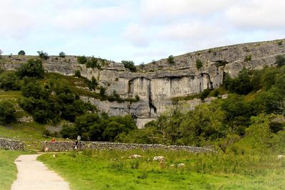 Scenic view of cliff by trees against sky