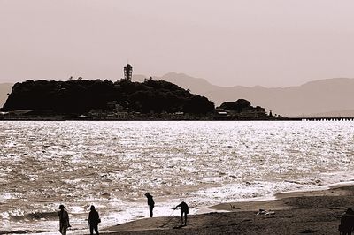 Silhouette people on beach against clear sky