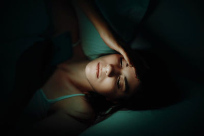 High angle view of woman using phone while lying on bed in darkroom