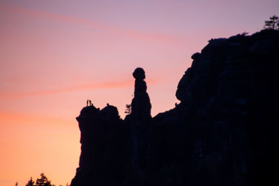 Silhouette man on rock against sky during sunset