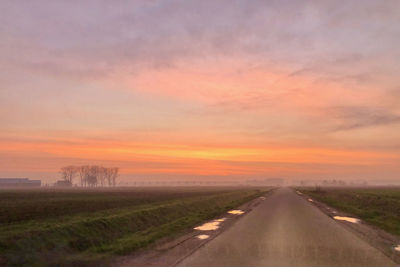 Road amidst field against sky during sunset