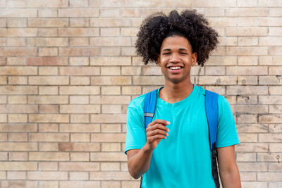 Afro latin male teenager smiling against a wall