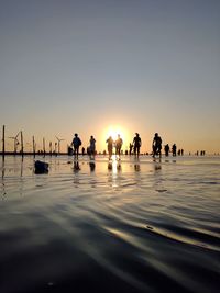 Silhouette people by sea against sky during sunset