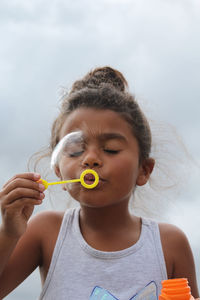 Girl blowing bubble while standing outdoors