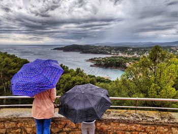 Rear view of woman and girl with umbrella by sea against sky