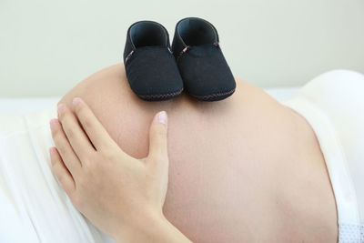 Midsection of pregnant woman with baby booties on abdomen lying on bed
