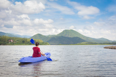 Rear view of woman kayaking in lake against sky