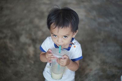 High angle portrait of cute baby boy drinking drink on floor