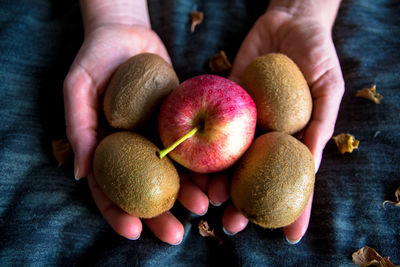 Cropped hands holding apple and kiwis on fabric