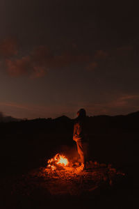 Side view of a woman watching a campfire under the stars