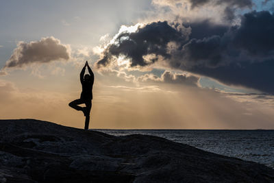 Silhouette woman practicing tree pose on sea shore during sunset