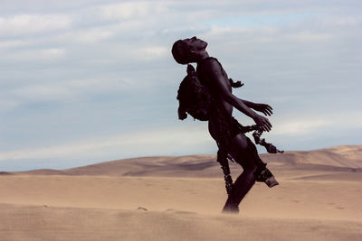 Model with costume wing standing at sandy desert against sky