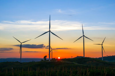 Wind turbines on land against sky during sunset