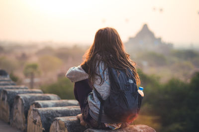 Rear view of woman sitting on retaining wall