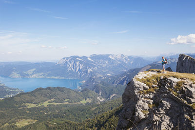 Full length of hiker standing on spinnerin peak while looking at attersee against blue sky