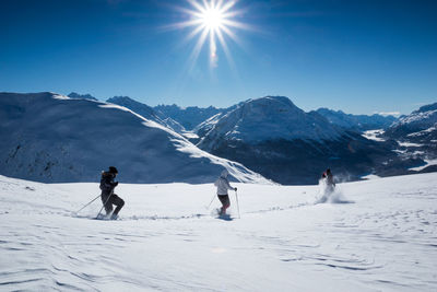 People skiing by snowcapped mountain against sky