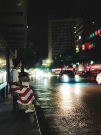 Rear view of people on illuminated street amidst buildings at night