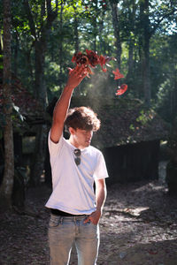 Young man throwing leaves while standing against trees in forest