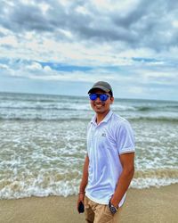 Man wearing sunglasses standing at beach against sky