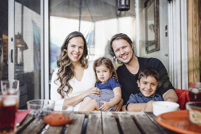 Portrait of happy family sitting against glass door outside house