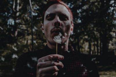 Close-up of man blowing dandelion while standing in forest