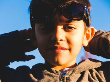 Portrait of cute boy with hands behind head standing against sky